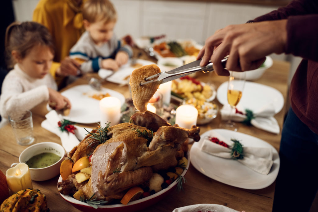 Close up of father serving Thanksgiving turkey during family dinner at dining table.